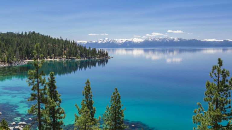 Picture of Lake Tahoe from east shore. There is a snow on the Sierra Nevada Mountains and some white clouds with reflection in turquoise waters of the lake.