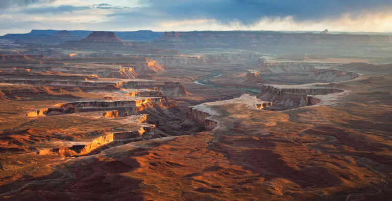 Sunset light breaks through storm clouds to illuminate the canyon walls below Green River Overlook in the Island in the Sky district of Canyonlands National Park, Utah.